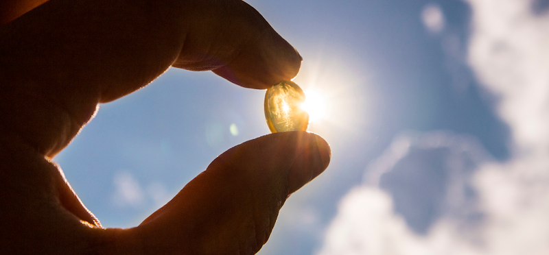 Hand holding up Vitamin D3 pill in sunlight